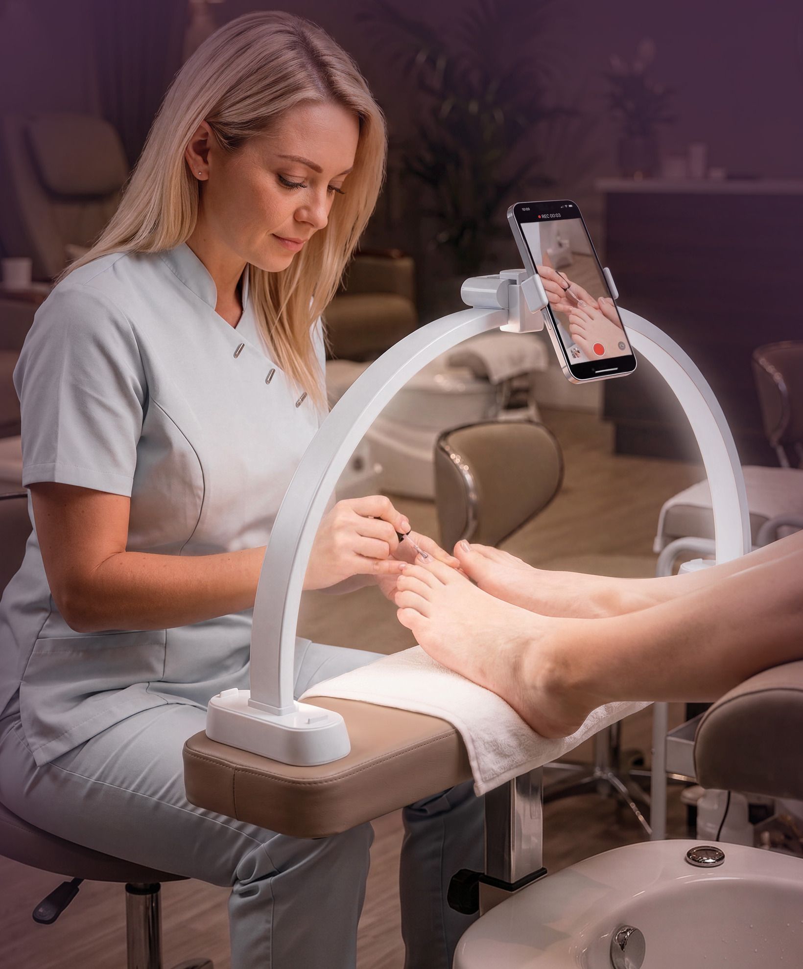A technician gives a pedicure under the white Half-Moon Light, with a phone in the phone holder.